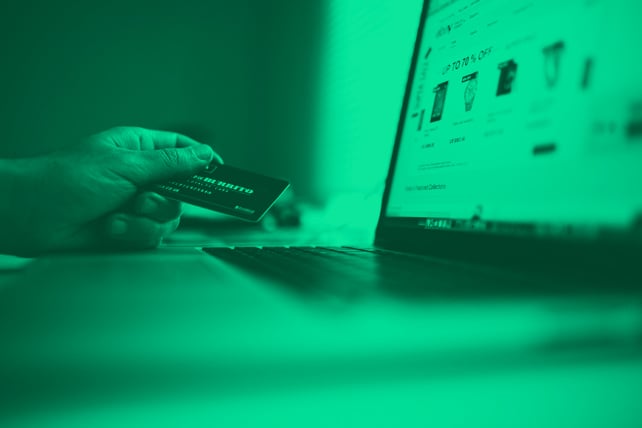 Person holding a credit card next to a laptop ready to buy a product they found through an e-commerce PPC ad