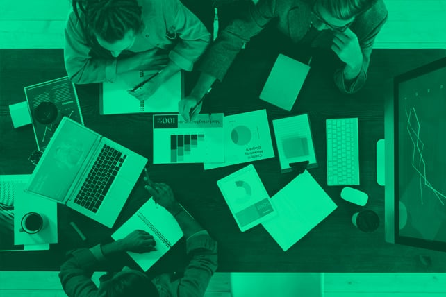 People in a digital marketing agency working around a desk with laptops and paper reports