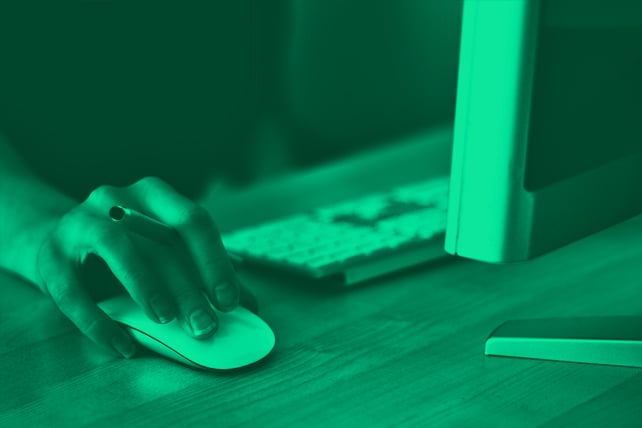 Woman using a computer with her hand on the mouse holding a pen